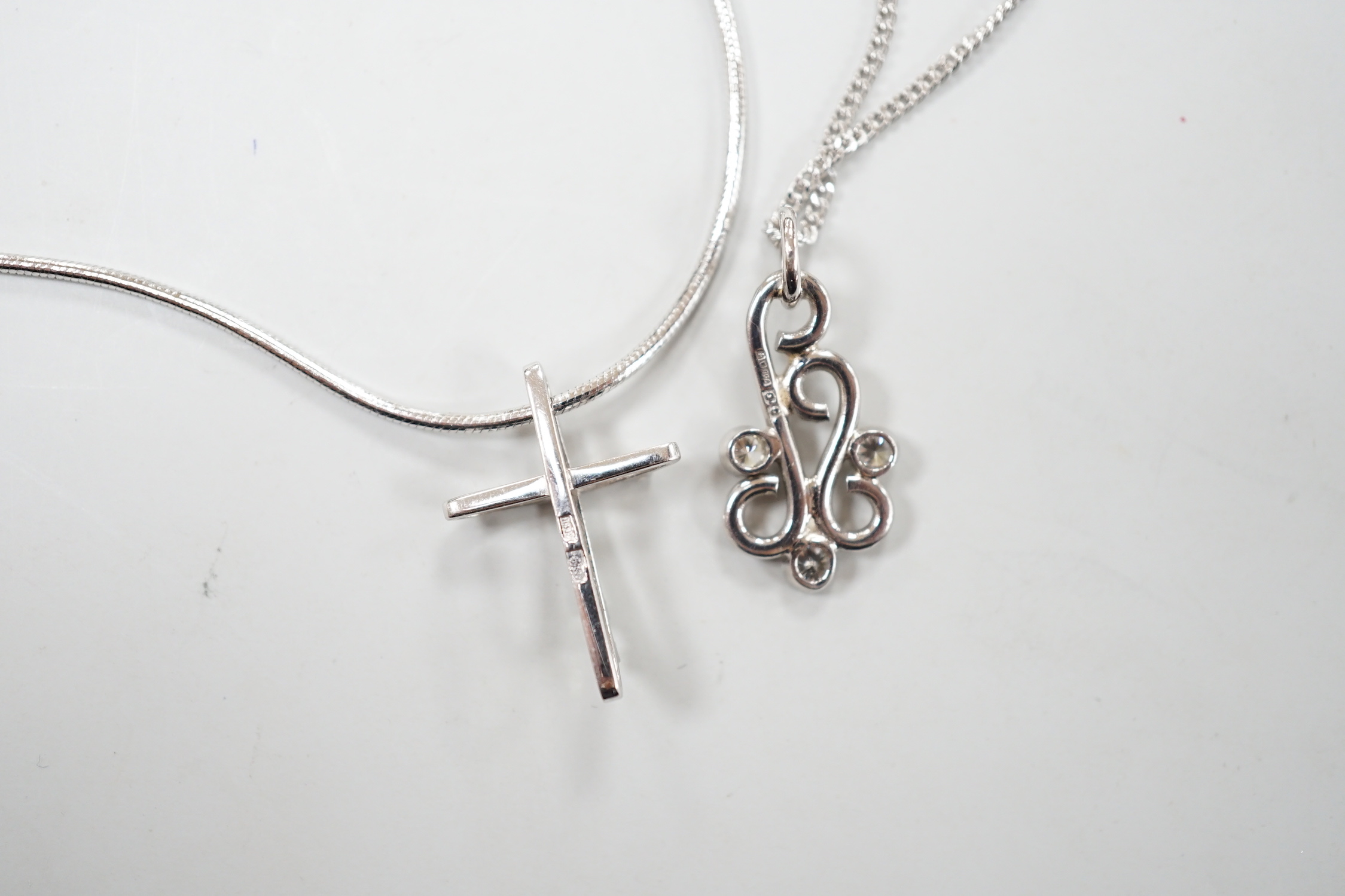 A modern 18ct white gold and three stone diamond set scroll pendant, 20mm, on an 18ct white gold chain, 39cm, gross weight 5.3 grams, together with a 585 white metal and diamond chip set cross pendant, on a 585 white met